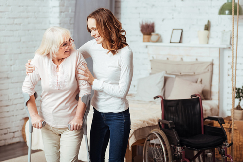 Daughter assisting mother with walking crutches standing next to wheelchair