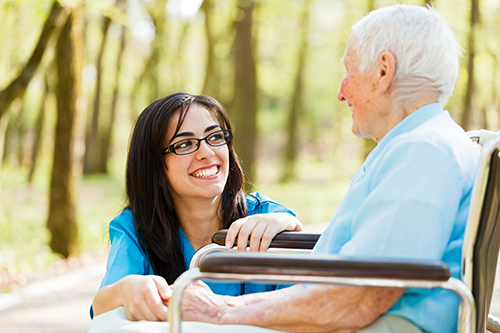 Young Nurse in blue scrubs knelt down smiling at elderly woman in wheelchair